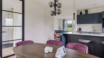 A modern kitchen with dark cabinets, a central island, and a dining area with a wooden table and purple chairs.