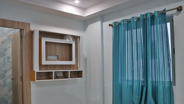 A bedroom with a bed, a wooden cabinet, and a teal curtain. - SSV TOP (Devanahalli)