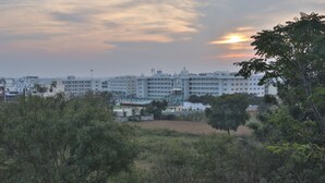 A large building with multiple floors and a prominent dome, surrounded by greenery and other buildings. - SSV TOP (Devanahalli)