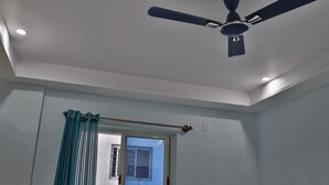 A room with a ceiling fan, a window with curtains, and recessed lighting. - SSV TOP (Devanahalli)