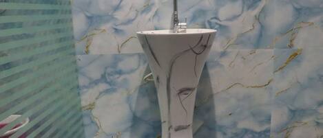 Un baño con pared de diseño de mármol y lavamanos sobre pedestal.