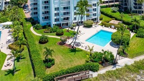 Ein mehrstöckiges Hotel mit Schwimmbad, umgeben von gepflegten Gärten und Palmen.