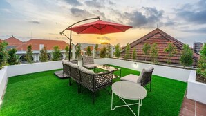 A rooftop patio with artificial grass, outdoor furniture, and a red umbrella. - Villa Nora by Five Elements (Canggu)