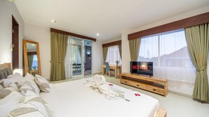 A hotel room with a large bed, a TV on a wooden stand, a desk with a chair, and a view of the outdoors through the windows. - Villa Nora by Five Elements (Canggu)