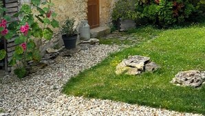 A rustic stone house with a wooden door, a small window, and a garden with flowers and greenery. - Charming house in the heart of the Vexin Normand 1 hour from Paris and 20 mn from Giverny (Vexin-sur-Epte)