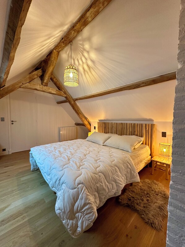 A spacious attic bedroom with a large bed, wooden beams, and a sloped ceiling.