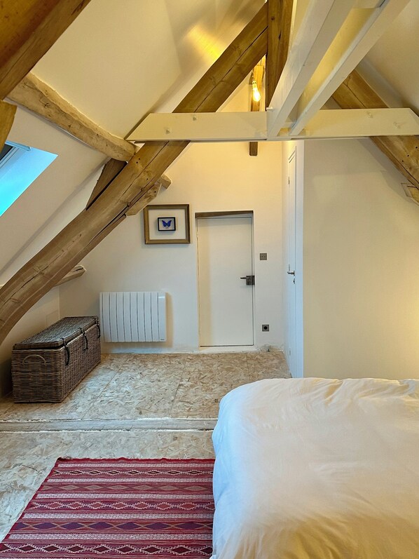 Een slaapkamer met schuine balken, een bed, een rood tapijt met patroon, een rieten kist en een witte radiator.
