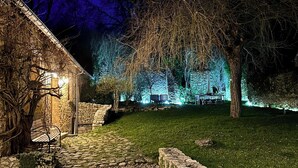A stone pathway leading to a rustic building with a bench and a table, surrounded by trees and illuminated by blue lights. - Charming house in the heart of the Vexin Normand 1 hour from Paris and 20 mn from Giverny (Vexin-sur-Epte)
