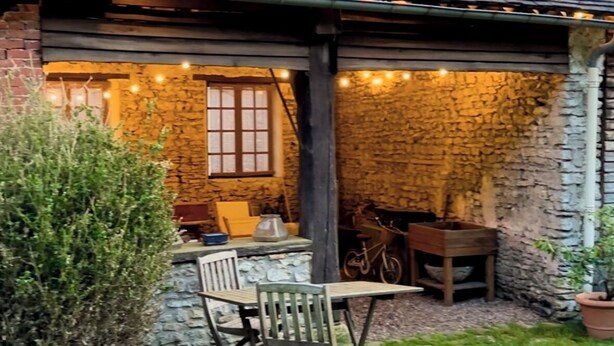 A rustic stone building with a tiled roof, a small outdoor seating area with a wooden table and chairs, and a stone wall with a window. - Charming house in the heart of the Vexin Normand 1 hour from Paris and 20 mn from Giverny (Vexin-sur-Epte)