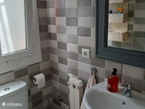 Ein Badezimmer mit gefliesten Wänden, Toilette, Waschbecken und Spiegel.