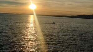 Een zonsondergang boven een rustig wateroppervlak met een verre kustlijn.