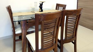 Un comedor con una mesa redonda, cuatro sillas de madera y un reloj montado en la pared.