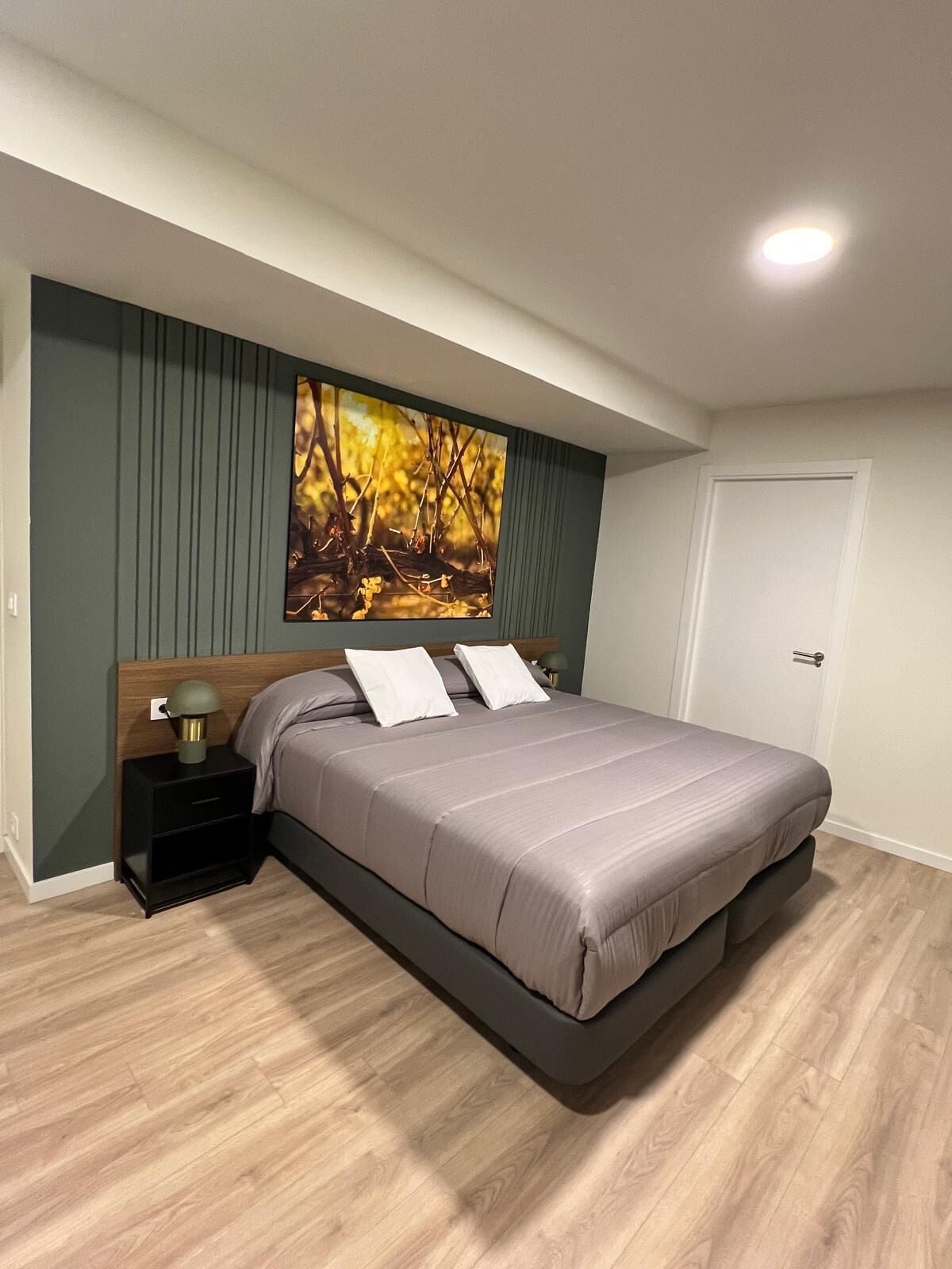 A bedroom with a bed, a nightstand, a wall-mounted painting, and a door.