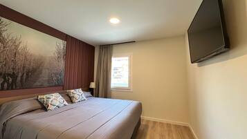 A bedroom with a bed, a TV mounted on the wall, a window with curtains, and a painting on the wall.