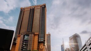 Un immeuble moderne de grande hauteur, sur lequel on peut voir un grand panneau indiquant « BERUVA TIMES SQUARE », entouré d’infrastructures urbaines et bordé par une rue animée.