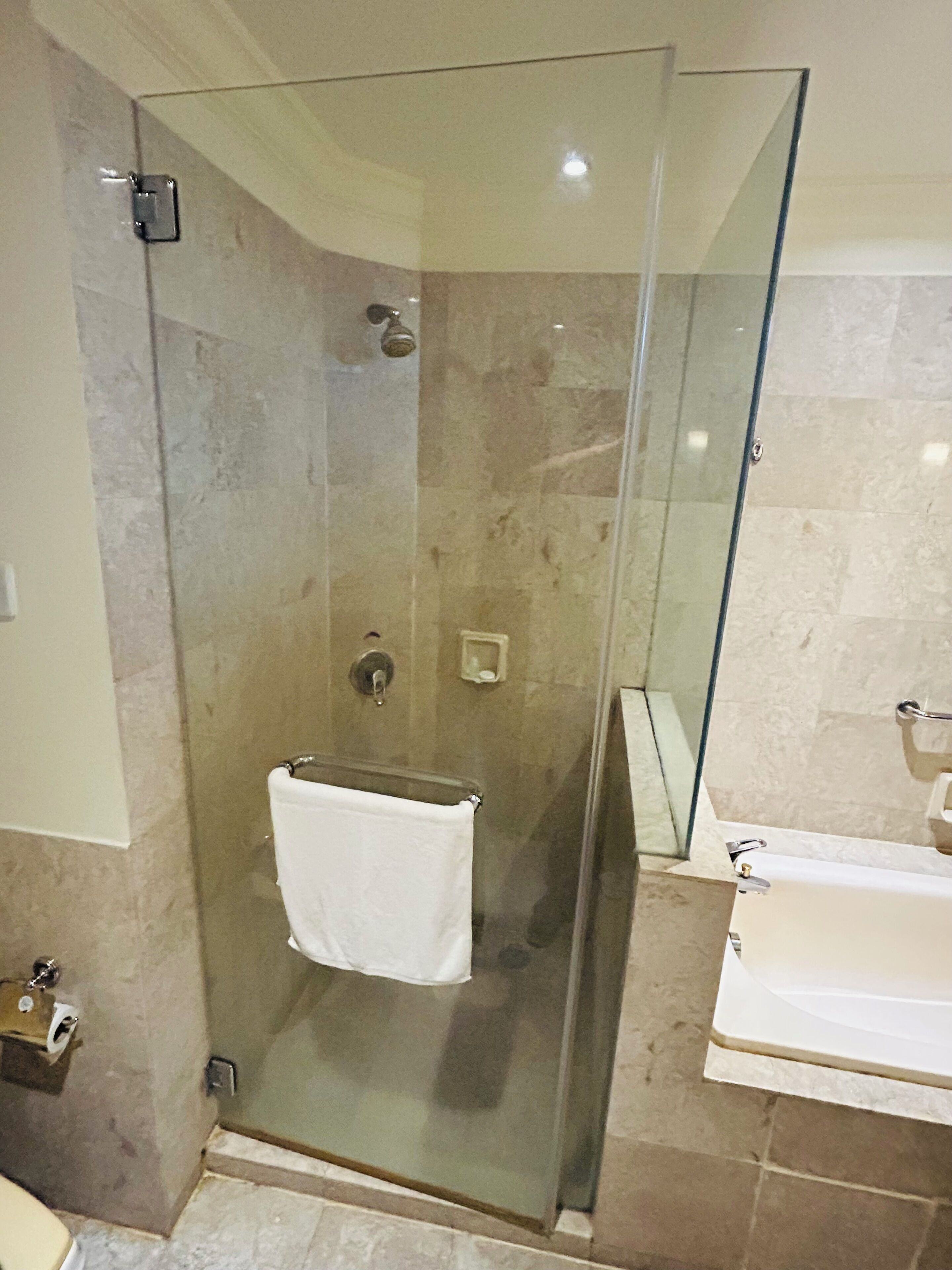 A glass-enclosed shower stall with a white towel hanging on a rack, a glass door, and a white sink with a mirror.