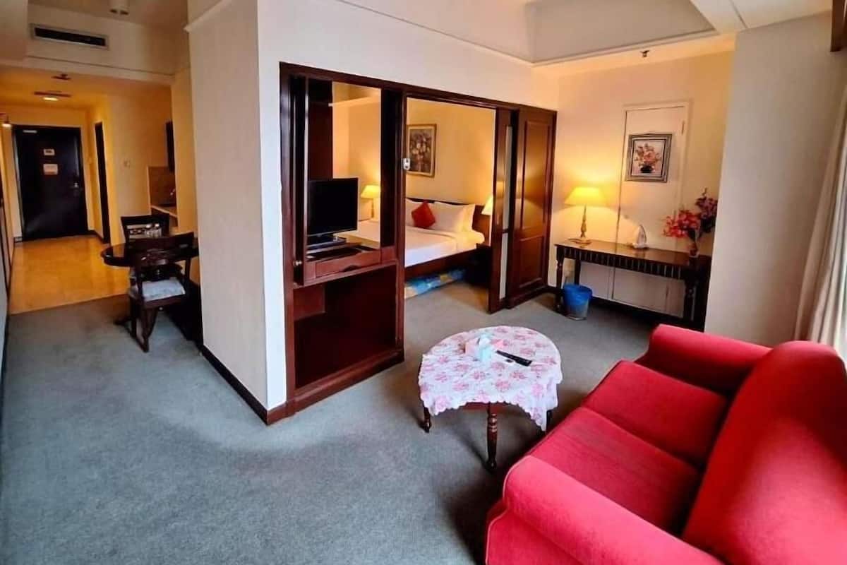 A hotel room with a bed, a desk, a chair, a red sofa, and a small round table.