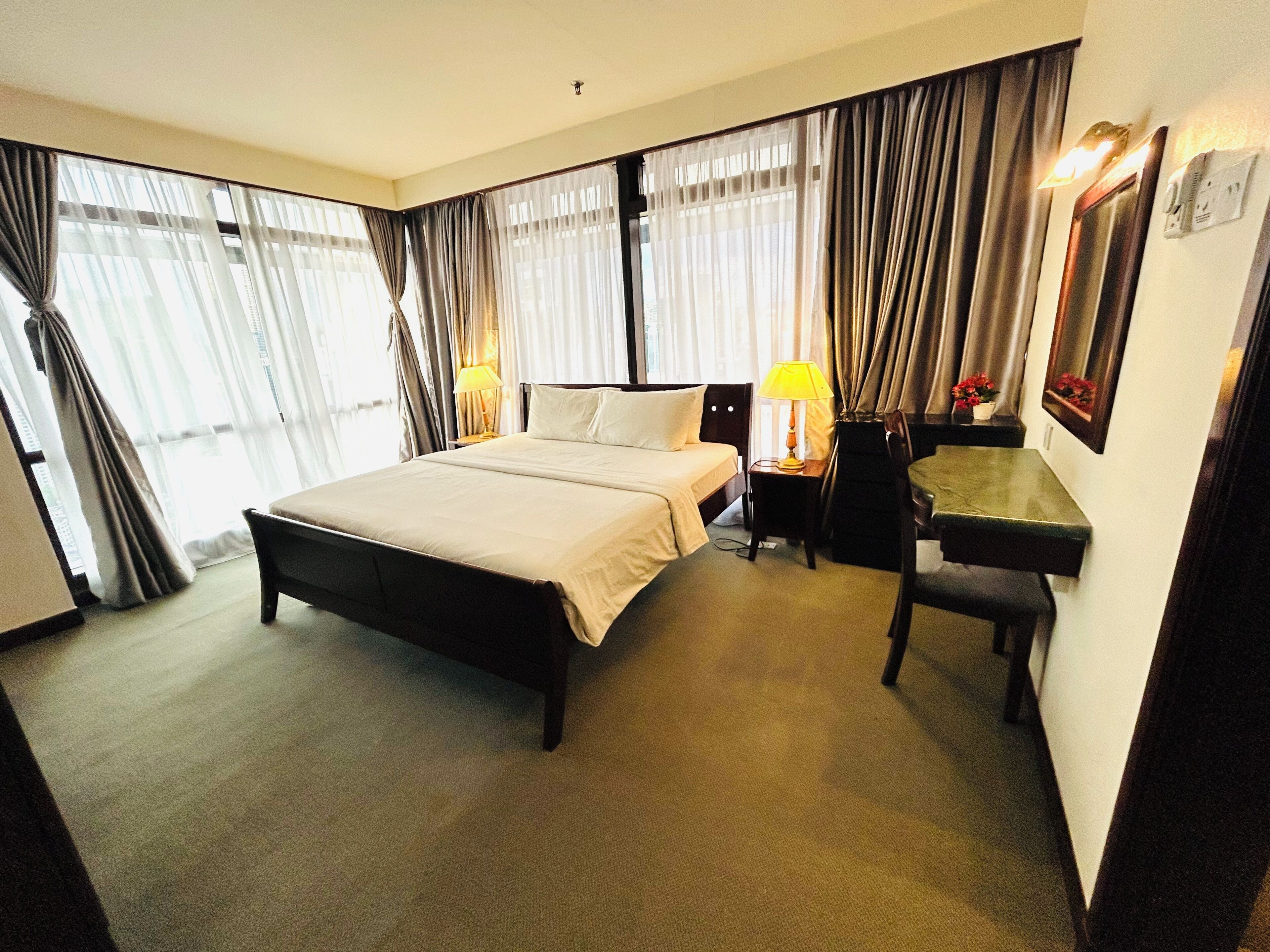 A hotel room with a large bed, a desk, a chair, and a lamp.