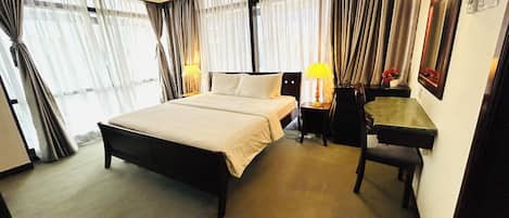 Quarto de hotel com uma cama grande, uma escrivaninha, uma cadeira e um abajur.