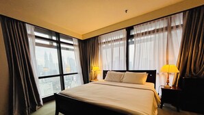 Une chambre d’hôtel avec un grand lit, deux lampes de chevet et une vue sur le paysage urbain, grâce à de grandes fenêtres dotées de rideaux.