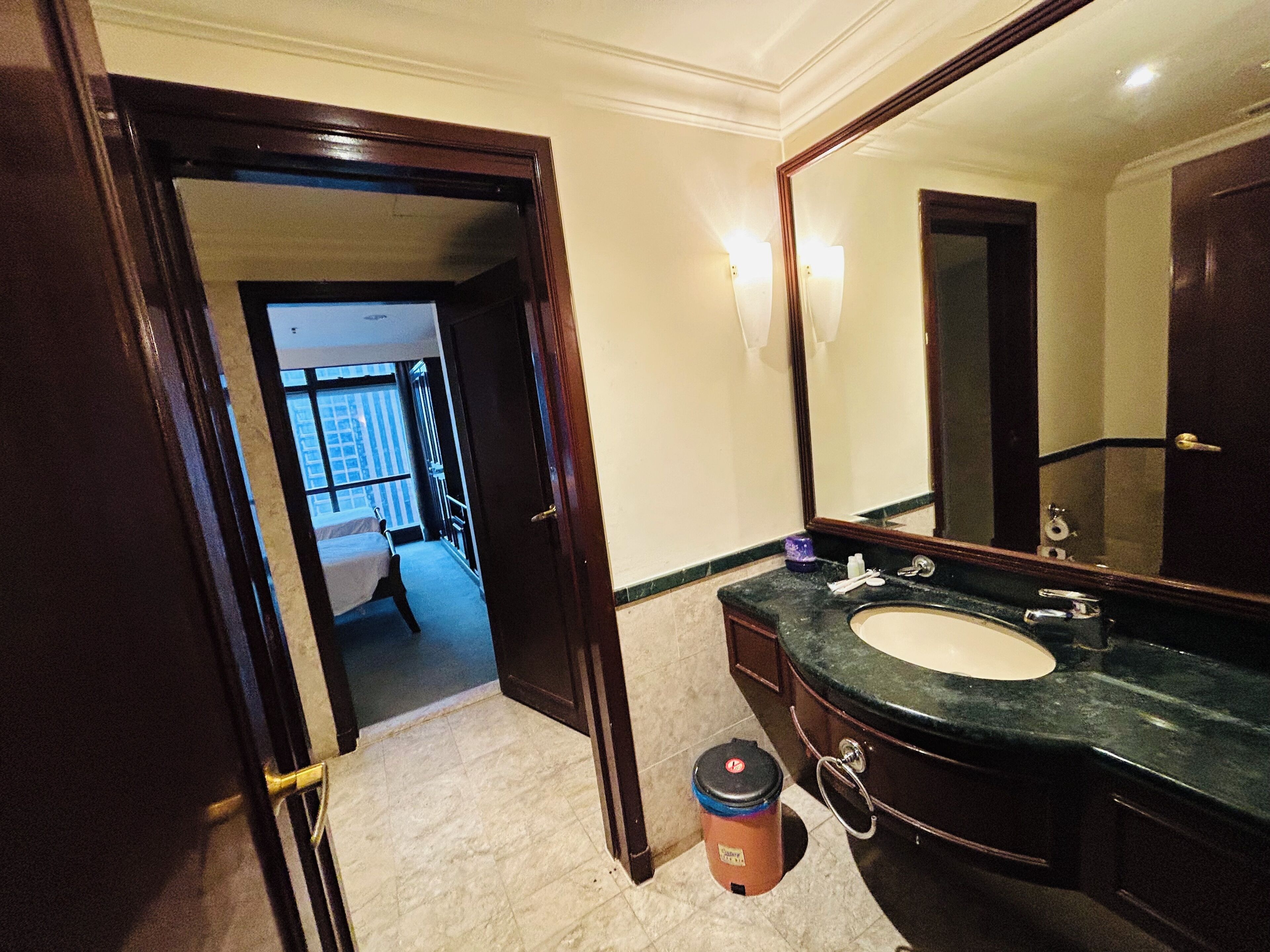 A hotel bathroom with a large mirror, a sink, and a trash can.