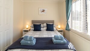 Un letto ben rifatto con due cuscini, un quadro appeso al muro e una finestra con tende.