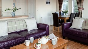 Een gezellige woonkamer met een paarse zithoek, een houten salontafel met theeservies, en een eethoek met tafel en stoelen.