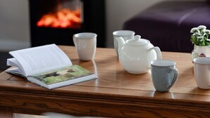 Een houten tafel met een boek, theepot, kopjes en een kleine plant in een pot.