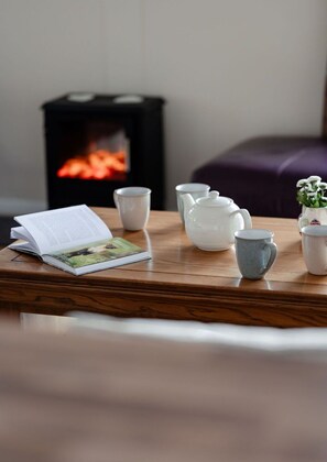 Een houten tafel met een boek, theepot, kopjes en een kleine plant in een pot.