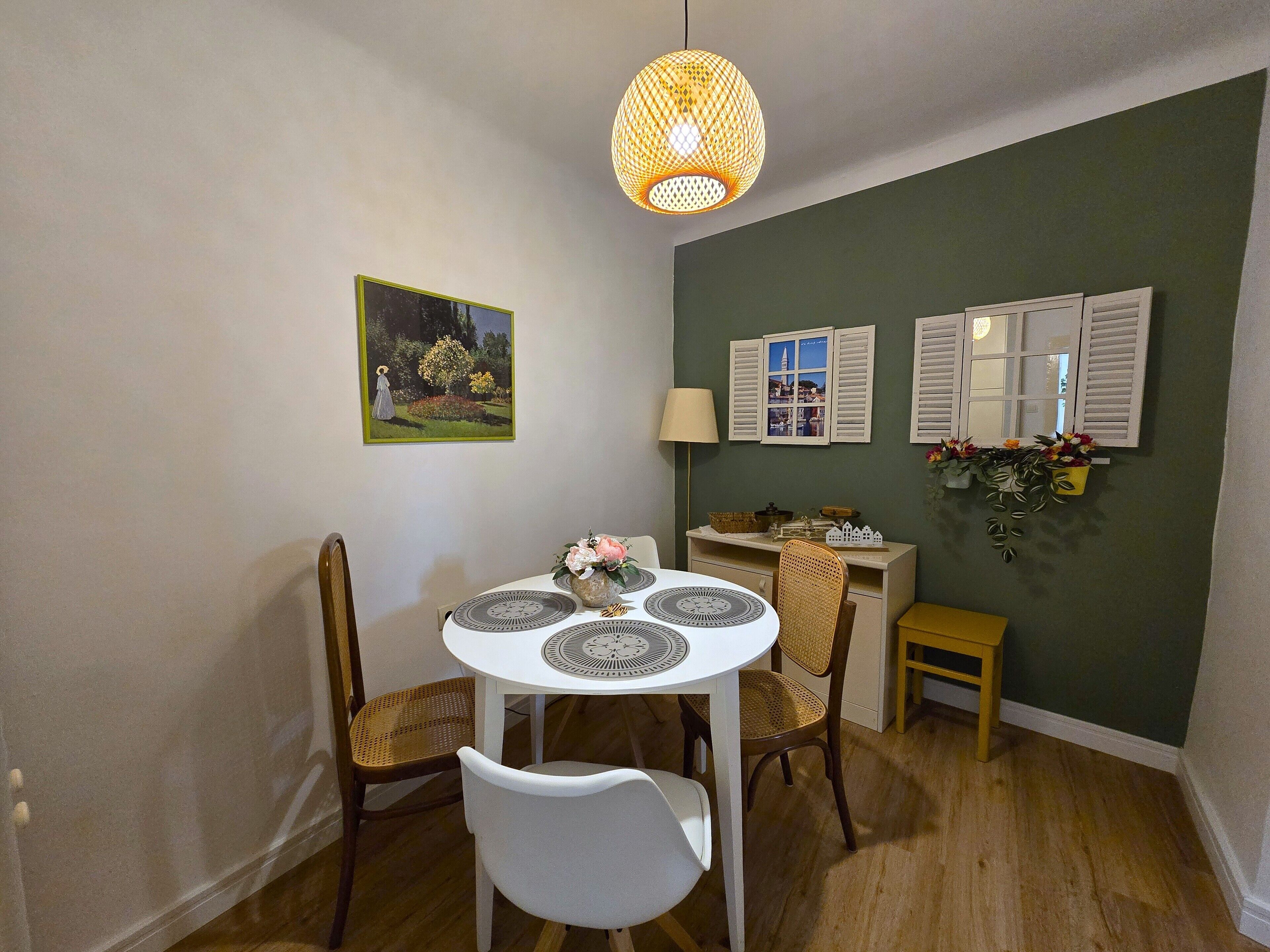 A dining area with a round table, two chairs, a hanging light fixture, a small side table, and wall-mounted decorations.