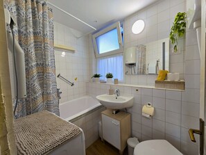 A bathroom with a bathtub, sink, toilet, and a window. - Two-Bedroom Apartment SEVEN (Rovinj)