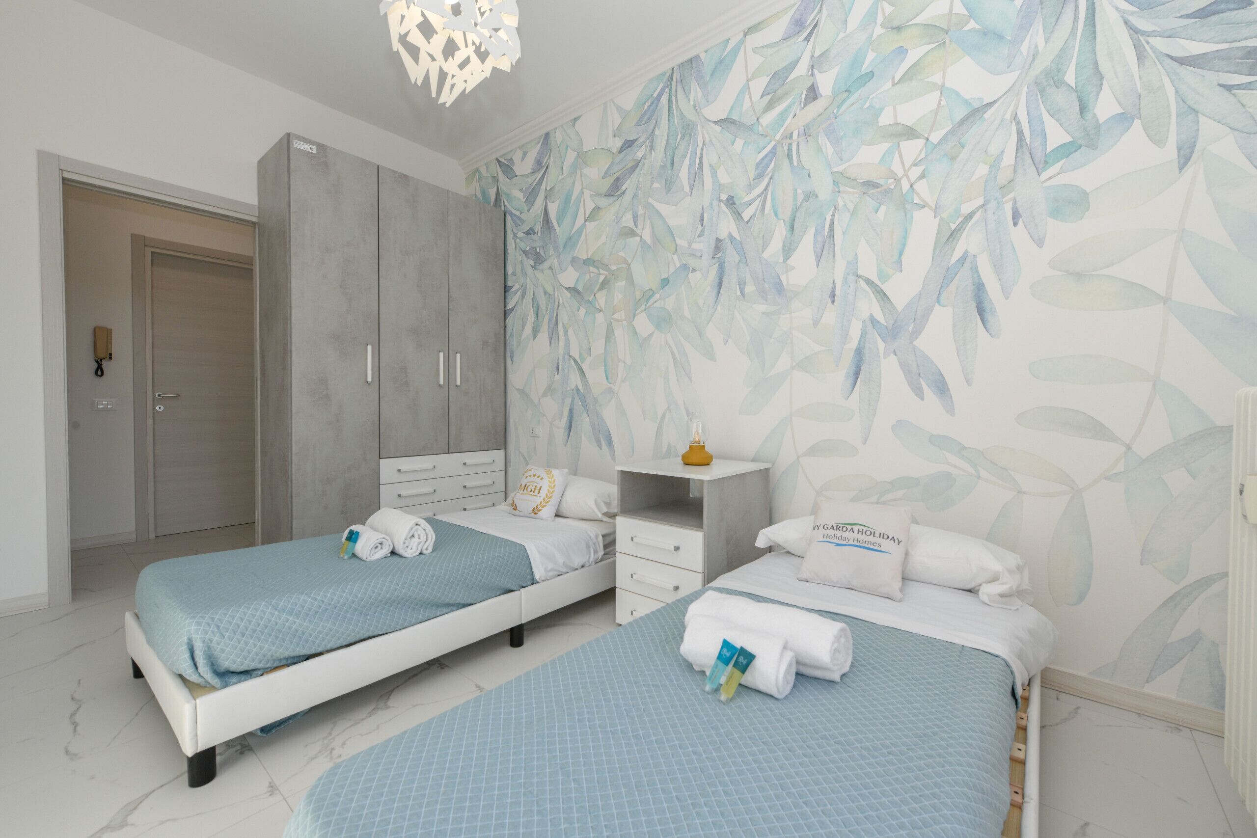 Une chambre d’hôtel avec deux lits, une armoire, un bureau et un mur orné d’un motif de feuilles.