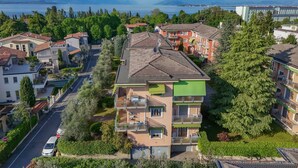 Un immeuble résidentiel à plusieurs étages, doté de balcons, entouré de verdure et offrant une vue sur un lac et des montagnes.