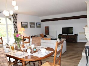 Un comedor con una mesa de madera dispuesta para cuatro personas, un sofá y un televisor al fondo.