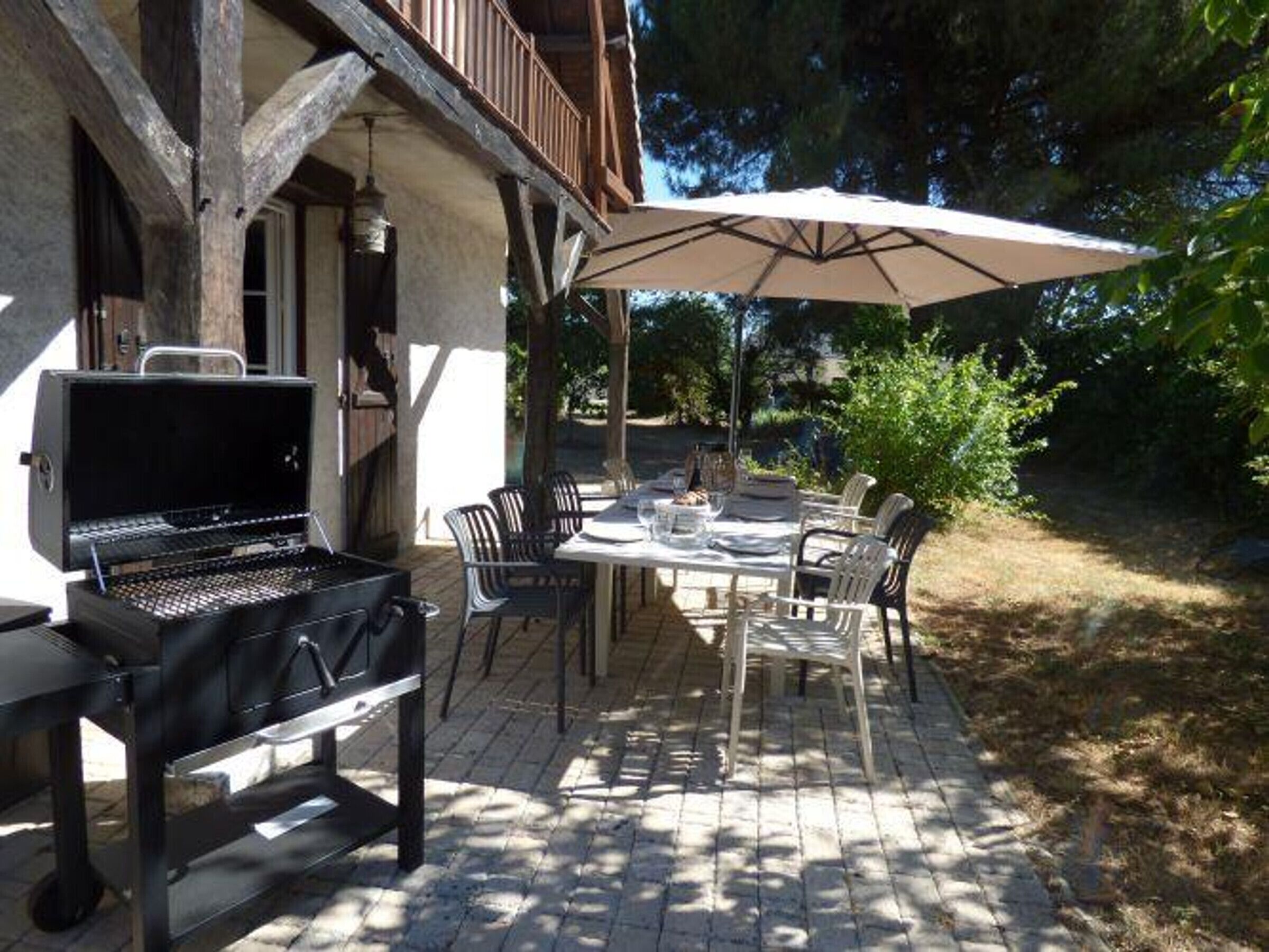 Une terrasse extérieure équipée d’un barbecue, d’une table à manger, de chaises et d’un parasol.