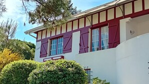 Un edificio de dos pisos con fachada blanca y contraventanas rojas.