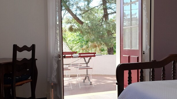 Una habitación con una cama, una silla de madera y vistas a un patio al aire libre con mesa y sillas.