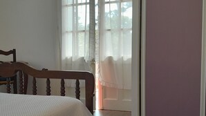 Un dormitorio con estructura de cama de madera, colcha blanca y puerta de vidrio corredera que da a un balcón.