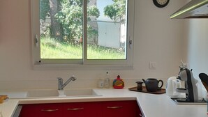 Una cocina con ventana, lavamanos, armarios rojos y varios electrodomésticos.