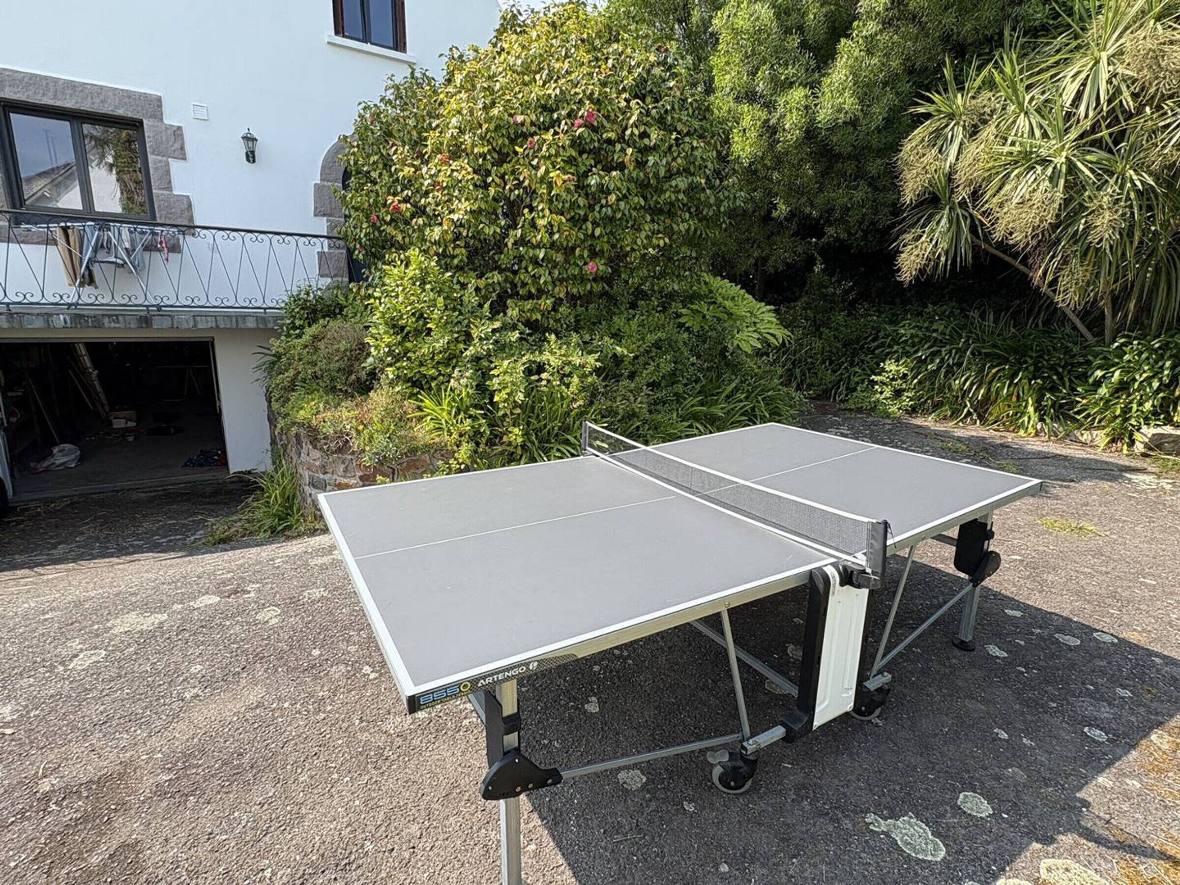 Deux tables de ping-pong ont été installées à l’extérieur, devant un bâtiment à la façade en pierre et doté d’un balcon.
