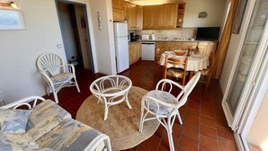 A compact kitchen with wooden cabinets, a refrigerator, and a microwave. There is a dining area with a round table and four chairs. - 2-room Apartment - Sea View - Pool - Cavalaire (Cavalaire-sur-Mer)