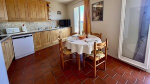 A compact kitchen with wooden cabinets, a white dishwasher, and a dining table set for four. - 2-room Apartment - Sea View - Pool - Cavalaire (Cavalaire-sur-Mer)