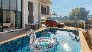 Una casa moderna con piscina, muebles de exterior y un SUV rojo estacionado afuera.