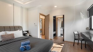 Un dormitorio moderno con una cama grande, un escritorio y una silla. Se ve un armario y un baño a través de una puerta abierta.