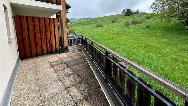 Een balkon met houten spijlen dat uitkijkt over een groen veld.