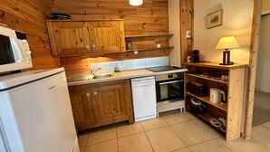 A compact kitchen with wooden cabinetry, a microwave, a dishwasher, an oven, and a sink. - Cozy apartment in Villard-de-Lans, 4 people, 52 m² (Villard-de-Lans)
