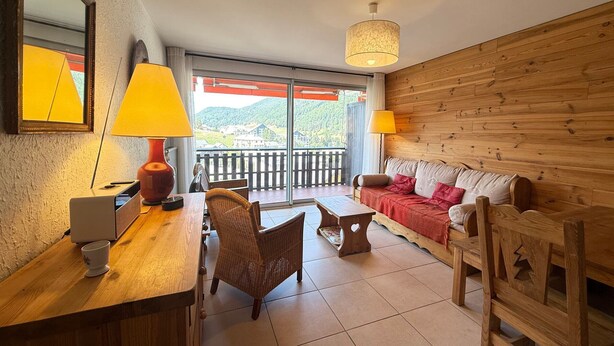 A cozy room with a wooden sofa, a dining table, and a laptop. There is a balcony with a view of the mountains. - Cozy apartment in Villard-de-Lans, 4 people, 52 m² (Villard-de-Lans)