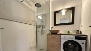 A modern bathroom with a glass-enclosed shower, a built-in washing machine, and a wooden vanity with a mirror above. - Cozy apartment in Villard-de-Lans, 4 people, 52 m² (Villard-de-Lans)