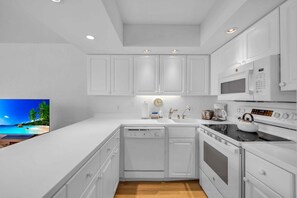 A modern kitchen with white cabinetry, a dishwasher, an oven, a microwave, and a kettle.