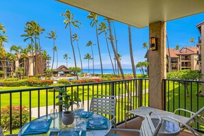 A balcony with a table, chairs, and a view of the ocean and palm trees.
